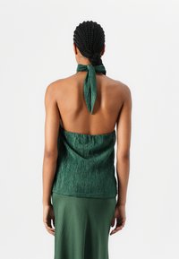 Top verde senza maniche in tessuto testurizzato, con un laccio sulla schiena e un design aperto sul retro, abbinato a una gonna verde coordinata.