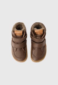 Stivaletti per bambini in pelle marrone con cinturini in velcro, foderati in pelliccia, suole in gomma e texture liscia. Gli accenti includono una toppa in pelle beige sulla linguetta.