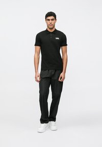 Čierna polokošeľa s krátkymi rukávmi a golierom, s bielym logom. Kombinovaná s čiernymi nohavicami a bielymi teniskami.