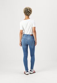 Smalje bukser i medium blå denim med høj talje, parret med en tætsiddende hvid skjorte. Har baglommer og et brunt læderlogo.