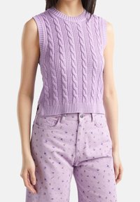 Hihaton laventelinvärinen palmikkoneule, jossa on ribbireuna, yhdistettynä laventelinvärisiin housuihin, joissa on pieniä kukkakuvioita violetilla ja kultaisella korostuksella.