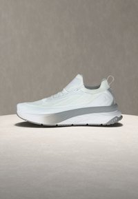 Λευκό αθλητικό παπούτσι με πλεκτό επάνω μέρος, μαλακή χοντρή σόλα, ταινία για το τράβηγμα στη φτέρνα και λογότυπο EA7 στο πλάι της σόλας, εμφανιζόμενο σε ουδέτερη επιφάνεια.