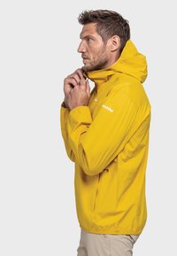 Gelber wasserdichter Mantel mit Kapuze, Reißverschluss vorne und Seitentaschen. Glatte Textur und leichtes Design. Markenlogo am Ärmel.