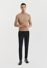 Beżowy sweter golf, dopasowany, w połączeniu z czarnymi dopasowanymi spodniami i czarnymi botkami za kostkę. Prosty design, gładka faktura, neutralne kolory.