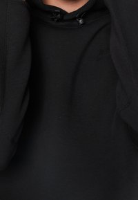 Svart sweatshirt med hög krage, dragsko och mjuk textur. Har flatlock-sömmar och en diskret logodetalj på bröstet.