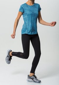 Blå kortärmad sporttop med ett strukturerat mönster, i kombination med svarta åtsittande leggings med meshdetaljer och grå träningsskor.