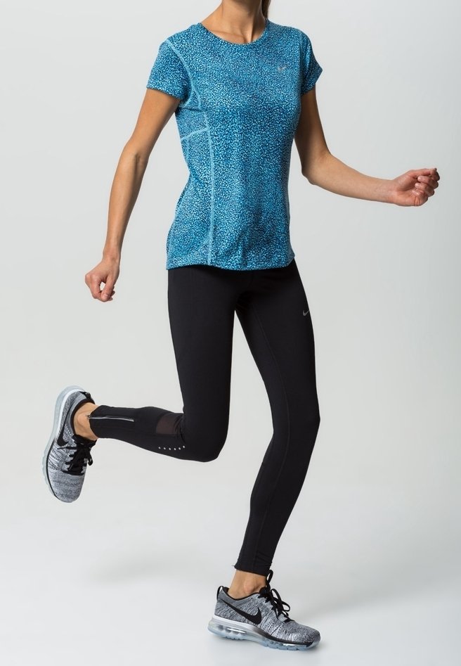 Blå kortärmad sporttop med ett strukturerat mönster, i kombination med svarta åtsittande leggings med meshdetaljer och grå träningsskor.