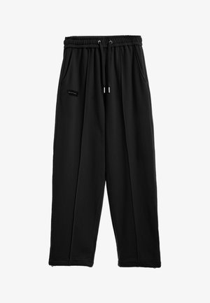 Pantalones jogger negros de corte holgado con cintura elástica, cordón, bolsillos laterales y una pequeña etiqueta rectangular con logo en el muslo izquierdo.
