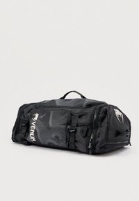 Must tekstuuriga spordikott, millel on lukud, reguleeritavad rihmad ja silmapaistev logo. Valmistatud vastupidavast nailonmaterjalist.