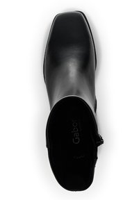 Svart läderankelskänga med fyrkantig tå, slät yta, sidodragkedja och vadderad insida. Varumärkeslogotyp synlig invändigt.