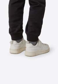 Valkoiset nahkakengät, joissa on pehmustettu kaulus ja kieli, kuvioitu ulkopohja, tarranauha ja minimalistinen muotoilu.