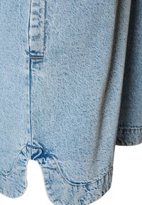 Svetlomodrá džínsovina s detailným prešitím a pútkom na opasok, zobrazujúca textúru a švové línie na okraji odevu.