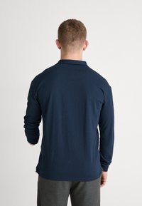 Granatowa koszula polo z długim rękawem, z kołnierzykiem, wykonana z miękkiej bawełny, z prostym dołem. Charakteryzuje się prostym wzorem i minimalnymi detalami przy szwach.