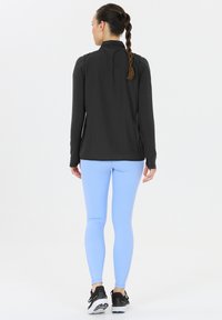 Svart långärmad idrottströja med hög krage, parat med ljusblå leggings. Slitstarkt tyg, figursydd design och minimal sömdetalj.