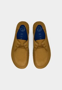 Ζευγάρι παπούτσια μοκασίνια από ταμπά σουέντ με μπλε σκούρο εσωτερικό και καφέ κορδόνια, απεικονισμένα από πάνω σε λευκό φόντο.