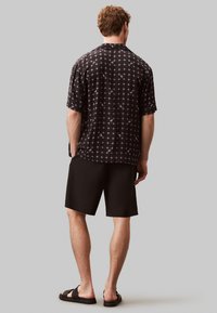 Maglietta nera a maniche corte con un motivo a griglia, dettagli bianchi, abbinata a pantaloni corti neri e sandali. Design casual, tessuto leggero.