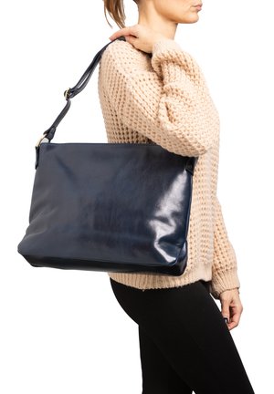 Borsa a mano in pelle blu navy con una superficie liscia, forma rettangolare e tracolla rimovibile, indossata di lato da una modella.
