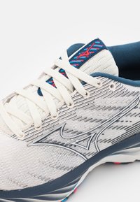 Scarpa da corsa leggera in bianco e blu navy. Presenta una tomaia in mesh testurizzato, lacci color crema, dettagli argentati e decorazioni colorate sulla linguetta.