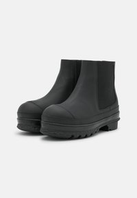 Black rubber ankle boots with a rounded toe, elastic side panels, and textured sole for grip. Smooth material with a matte finish.