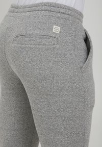 Gray joggers made of soft fabric, featuring a back pocket and logo tag near the waistband. The design includes a textured finish.