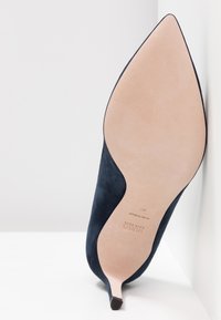 Marineblå ruskinds højhælet sko med spids tå og smal hæl, som har en glat nude sål. Markerede med "HUGO" og størrelse 37.