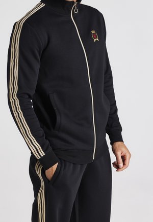 Zwarte zip-up trainingsjack met crèmekleurige strepen langs de mouwen. Heeft een hoge kraag en voorzakken. Gouden embleemdetail op de borst.