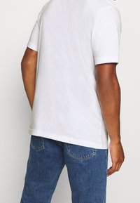 Vit t-shirt i bomull med korta ärmar, avslappnad passform och rundad halsringning, kombinerad med blå denimjeans med diskret sömnadsdetalj.