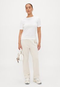 Top bianco a maniche corte abbinato a pantaloni crema. Gli accessori includono una piccola borsa bianca. Le scarpe sono grigio chiaro con accenti e motivi bianchi.