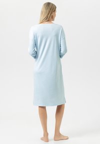 Jasnoniebieska, długa koszula nocna z długim rękawem o luźnym kroju, wykonana z miękkiego materiału, z okrągłym dekoltem i bocznymi rozcięciami przy dolnej krawędzi.