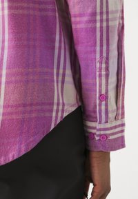 Purple plaid shirt made of woven fabric. Features a curved hem, buttoned cuffs with purple buttons, and light pink accent stripes.