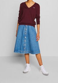 Vinröd v-ringad tröja, ljusblå jeanskjol i A-linje med knappar fram och vita höga sneakers med svarta detaljer.