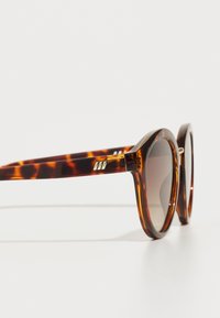 Ochelari de soare rotunzi cu un model de broască țestoasă, lentile gri și accente de metal auriu pe tempie. Cadru din policarbonat și un design elegant.