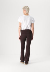 Brune flared bukser lavet af blødt stof med en bred talje; parret med en simpel hvid T-shirt, set fra ryggen.