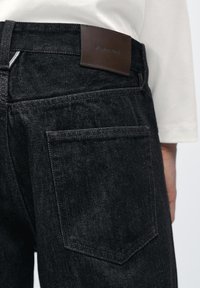 Sorte denimjeans med en struktureret pasform, med en brun læderbrandpatch og traditionelle baglommer med diskret syning.