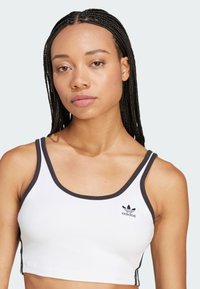 Witte crop top met zwarte randen en bandjes, met een klein zwart Adidas-logo aan de linkerkant, gemaakt van een gladde, rekbare stof.