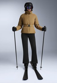 Ski outfit featuring a brown insulated jacket with a belt, black ski pants, black gloves, ski poles, and a black helmet with visor.