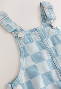 Lyseblå denimoveralls med ternet mønster, udstyret med metalclips og justerbare stropper. Tekstureret stof med synlige syningsdetaljer.