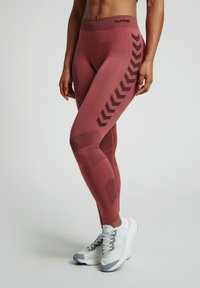 Hooggesneden, roestkleurige legging met zwarte geometrische patronen en textuuraccenten aan de zijkanten. Zachte, rekbare stof voor comfort.