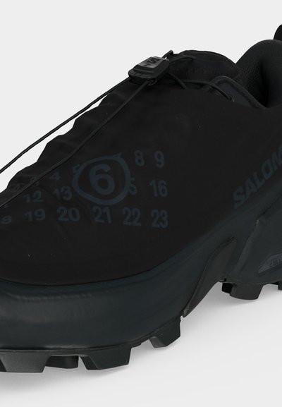 Μαύρο παπούτσι trail running Salomon με σύστημα γρήγορου κορδονιού και τυπωμένους αριθμούς, συμπεριλαμβανομένου ενός αριθμού 6 σε κύκλο στην επάνω πλευρά.