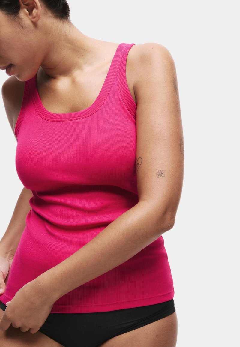 Tight rosa ribbad linne med rundad halsringning och breda axelband, kombinerat med svarta trosor. Slät textur, minimalistisk design.