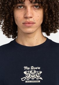 Sudadera azul marino con cuello de canalé, que presenta un gráfico central de tres calaveras con el texto "Los Hacedores" y "CONSTRUYE ALGO" abajo.