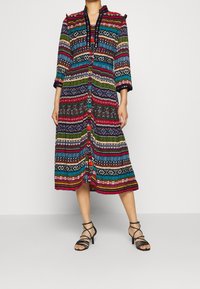 Robe midi multicolore présentant divers motifs géométriques, des manches longues, un devant à boutons et un tissu texturé. Accents et embellissements en noir.