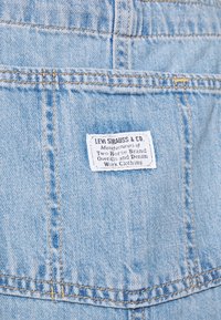 Tissu en denim bleu clair avec une poche arrière dotée d'une étiquette blanche Levi Strauss & Co. cousue avec du texte noir.