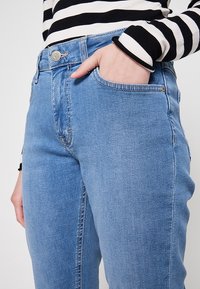 Los jeans de mezclilla azul claro presentan un diseño clásico con un bolsillo frontal, botón de metal plateado y costuras detalladas a lo largo de las costuras.