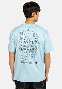 Camiseta de algodón azul cielo con un estampado gráfico negro en la parte posterior que presenta personajes y texto estilizados. Diseño de manga corta y cuello redondo.