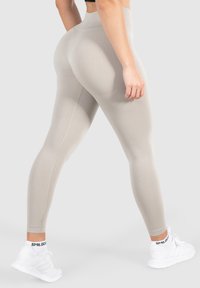 Lichtbeige high-waisted leggings met een gladde textuur, voorzien van zijnaad en gecombineerd met witte sportschoenen.