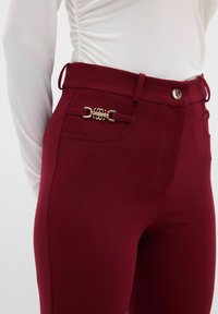 Bordeauxkleurige broek van soepel materiaal met gouden hardwareaccent en een getailleerd ontwerp met een hoge tailleband.