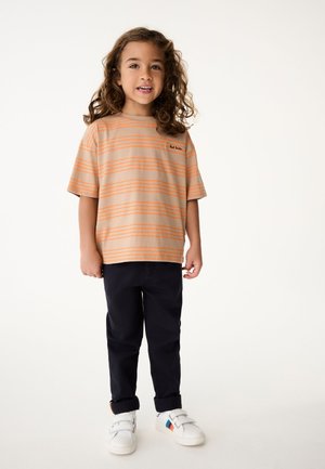 Stribet beige og orange kortærmet T-shirt, sorte bukser og hvide sko med velcro stropper og farvede detaljer.