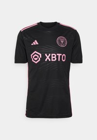 Musta jalkapallopaita, jossa vaaleanpunaiset korostukset, teksturoitu kuosi, pyöreä pääntie sekä joukkueen ja sponsorin logot edessä.