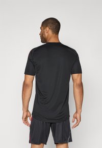 Sort atletisk T-shirt med korte ærmer, rund halsudskæring og en løs pasform, parret med sorte shorts med røde og hvide detaljer.